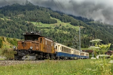 Der nostalgische Alpine Classic Pullman Express fährt durch eine grüne Landschaft.