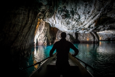 Eine Person in einem Boot auf einem unterirdischen See mit blauem Wasser in einer Höhle.