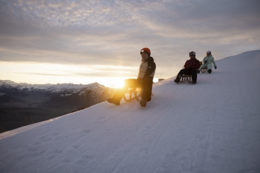 Three people are sledging down the hill at sunset.