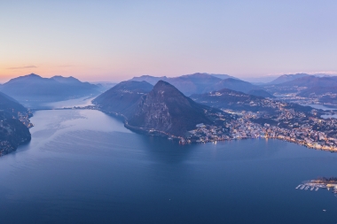 Vista su una città in riva al lago, circondata dalle montagne nell’atmosfera serale.
