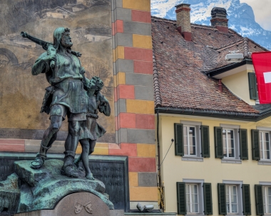 A statue in front of a historic building, next to a Swiss flag.