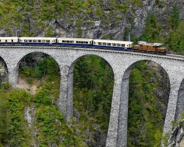 Un train sur un viaduc en pierre dans un paysage montagneux et boisé.