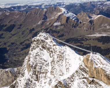 A snow-covered mountain peak with a suspension bridge and a Swiss flag.