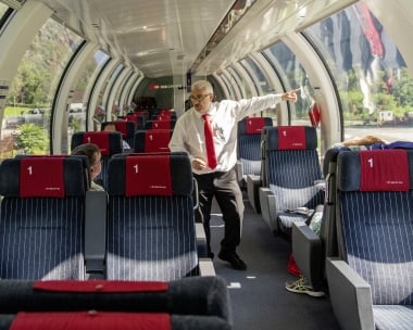 Un controllore indica qualcosa all'interno di un vagone moderno con finestre panoramiche.