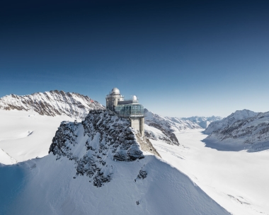 A research station on a snow-covered mountain peak under a blue sky.