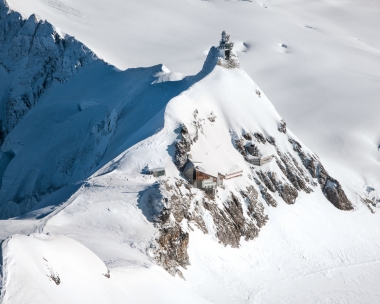 Eine verschneite Bergstation auf einem Gipfel mit umliegender Schneedecke.