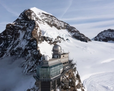 Eine Bergstation mit Observatorium vor einer verschneiten Berglandschaft.