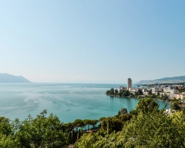 A city on the shore of a large lake with mountains in the background.