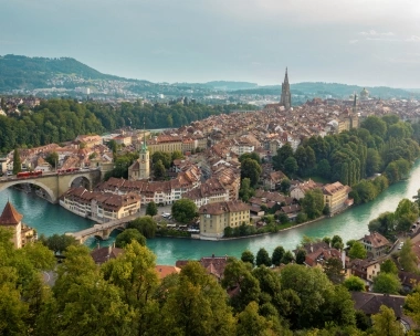 A city view of Bern, Switzerland, with the river Aare, historical buildings, and a large church in the background.