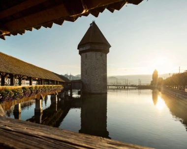 Eine alte Holzbrücke mit Blumen, daneben ein Wasserturm in der Abendsonne.