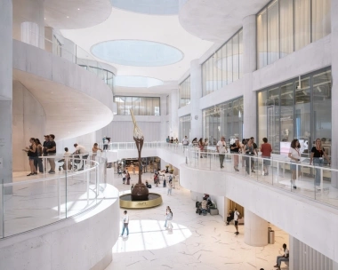 Une vue intérieure moderne et lumineuse d'un bâtiment à plusieurs étages avec des personnes en visite guidée et une grande sculpture en chocolat au centre.