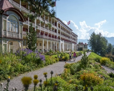 Une grande villa historique avec des toits rouges et un jardin dans un paysage fleuri.