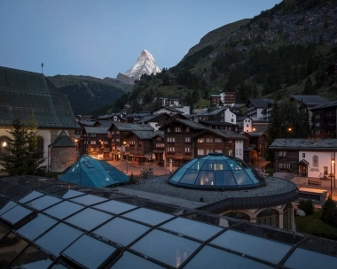 Blick auf ein Bergdorf mit traditionellen Häusern; im Hintergrund der Matterhorn bei Dämmerung.