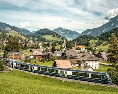 Eine idyllische Berglandschaft mit einem Zug, der durch ein malerisches Dorf fährt.