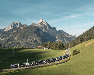 Train passes through green hills in front of a mountainous landscape.