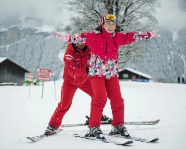 A ski instructor helps a student learn to ski in a snow-covered landscape.