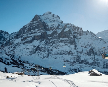 A snowy mountain landscape with a cable car in front of a large mountain range.