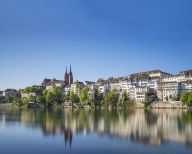 A city view by the river with historic buildings and a church in the background.