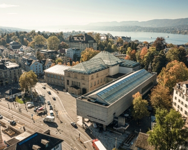 Aerial view of a large building complex in a city with a lake in the background.