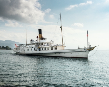Ein weisses Dampfschiff fährt auf einem See unter bewölktem Himmel.