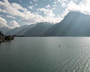 Un paysage lacustre paisible avec des montagnes en arrière-plan et des voiliers sur l'eau.