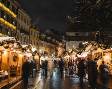 A festively lit Christmas market street with decorated stalls at night.