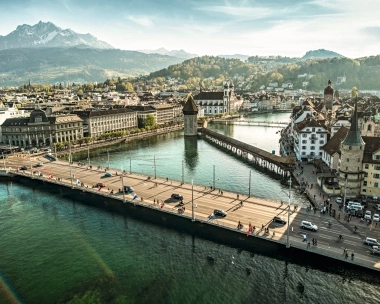 Aerial view of a historic bridge and old town with mountains in the background.