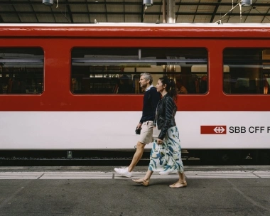 Two people walk past a red SBB train.