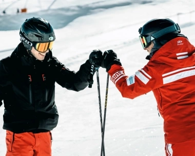 Deux skieurs sur une piste de ski se tapent dans la main.