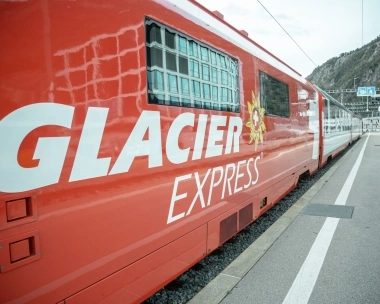 Ein roter Zug mit der Aufschrift "Glacier Express" steht am Bahnhof.
