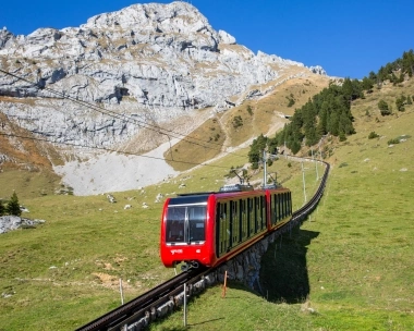 Eine rote Zahnradbahn auf einem steilen Schienenabschnitt in einer alpinen Landschaft.