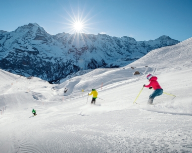 Drei Skifahrer auf einer sonnigen Piste vor einer beeindruckenden Bergkulisse.