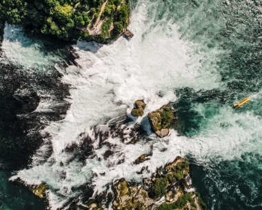 Aerial view of a large waterfall with rocks and a yellow boat on the water.