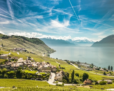 Eine malerische Landschaft mit einem Dorf, terrassierten Weinbergen und einem grossen See im Hintergrund.