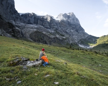 A person sitting in a meadow looking at an impressive mountain landscape.