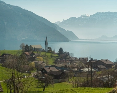 Eine idyllische Landschaft mit einer Kirche am See, umgeben von Bergen und Häusern.