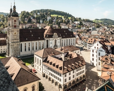 Aerial view of a historic church with surrounding buildings and hills in the background.