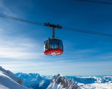 A cable car floats over snowy mountains and clear sky.