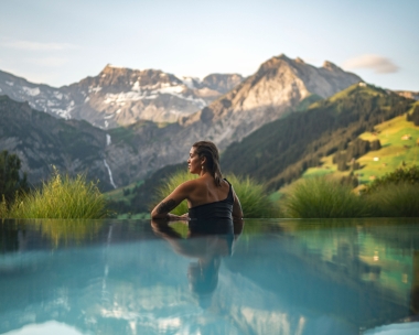 Eine Frau entspannt in einem Infinity-Pool mit Blick auf bergige Landschaft.