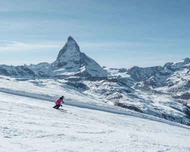 Une skieuse sur une piste enneigée avec le Cervin en arrière-plan.