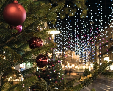 Christmas tree with red ornaments, with the glowing lights of a city street in the background.