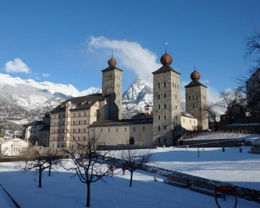 Castello con torri di fronte a montagne innevate e cielo blu.