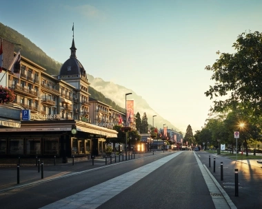 Breite Strasse mit historischen Gebäuden und Bergen im Hintergrund bei Sonnenuntergang.