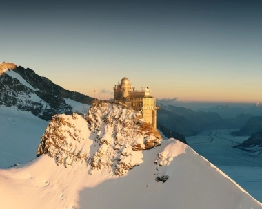 Observatorium auf verschneitem Berggipfel bei Sonnenuntergang.