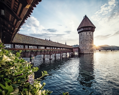 An old wooden bridge with a tower in the water at sunset.