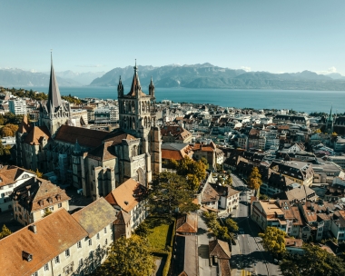 Aerial view of a historic church in a town with a lake and mountains in the background.