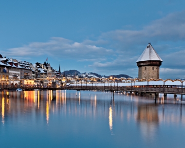 Eine historische Brücke und Gebäude am Fluss in der Abenddämmerung, mit Schnee bedeckt.