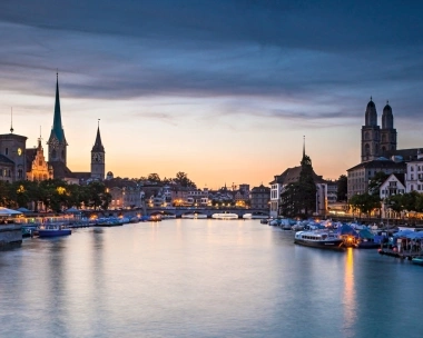 Coucher de soleil sur une ville avec une rivière, un pont et des bâtiments historiques.