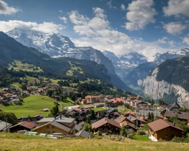 Villaggio di montagna in un paesaggio alpino con cime innevate sullo sfondo.