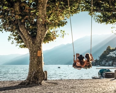 Two women sit on a swing and look out over the lake
